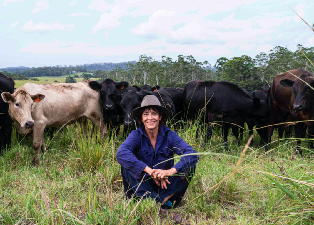 rachel ward sitting in grass on farm with cattle behind her