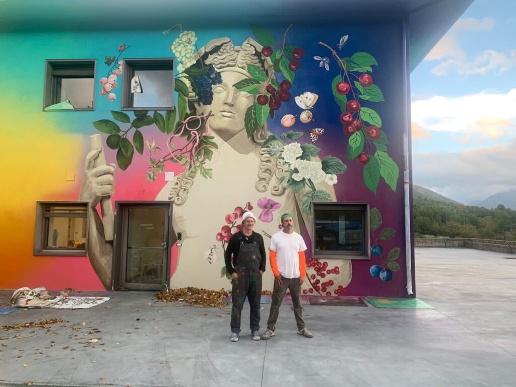 two artists standing in front of large mural